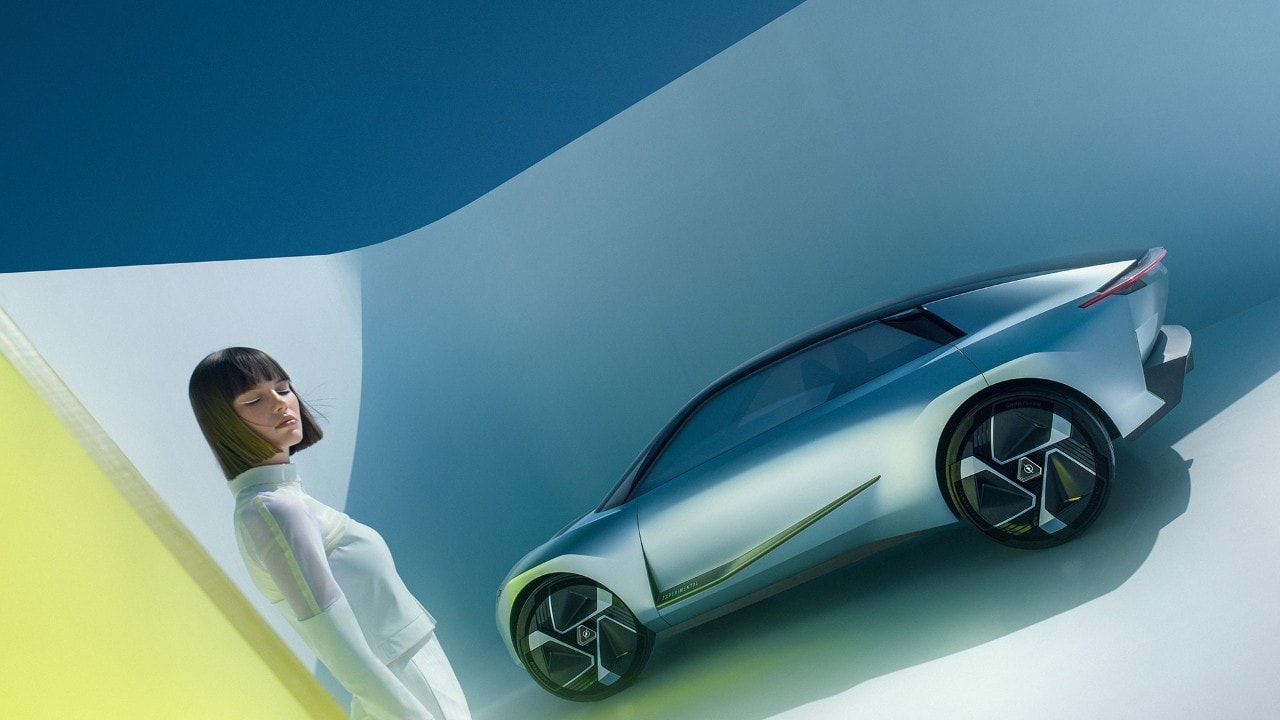 Vista lateral de un Opel Experimental plateado con una mujer al lado.